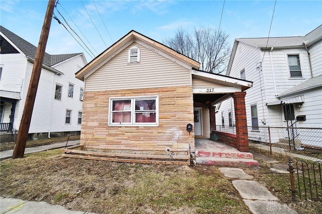 view of front of home with stone siding, a porch, and fence