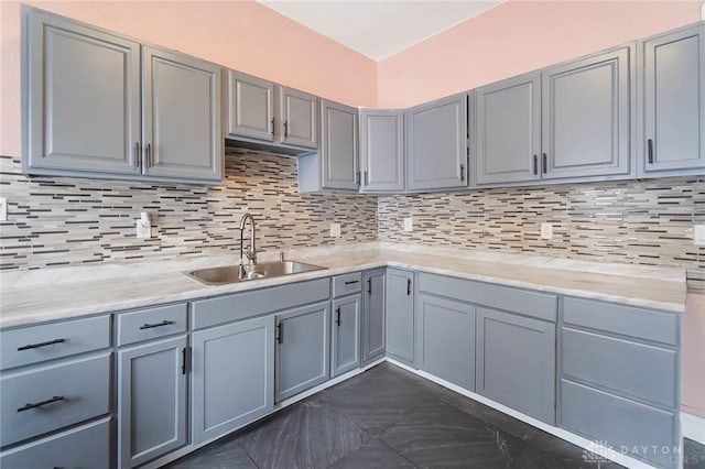 kitchen with gray cabinetry, tasteful backsplash, a sink, and light stone countertops