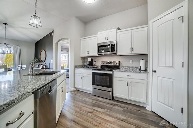 kitchen with arched walkways, light wood-style flooring, appliances with stainless steel finishes, hanging light fixtures, and a sink