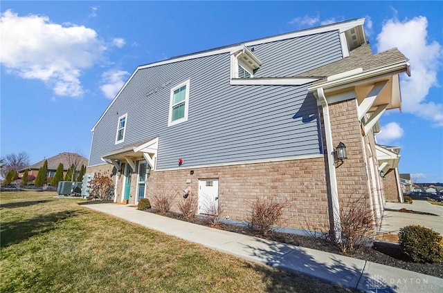 view of front facade featuring central AC, brick siding, and a front yard