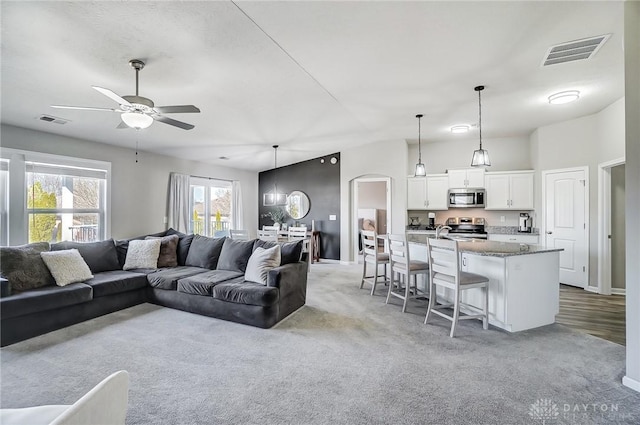 living room featuring arched walkways, visible vents, ceiling fan, and light carpet