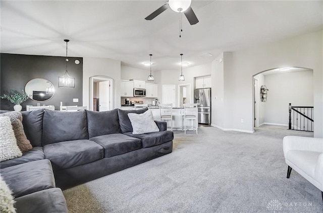 living area featuring baseboards, arched walkways, a ceiling fan, and light colored carpet