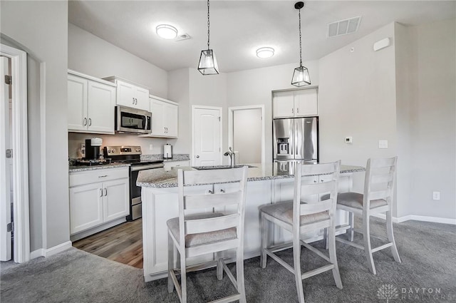 kitchen with visible vents, a breakfast bar area, a kitchen island with sink, stainless steel appliances, and a sink