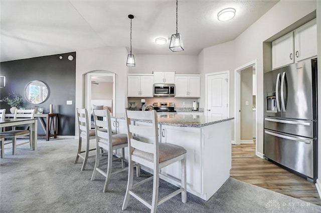 kitchen featuring light stone counters, arched walkways, stainless steel appliances, white cabinetry, and a kitchen breakfast bar