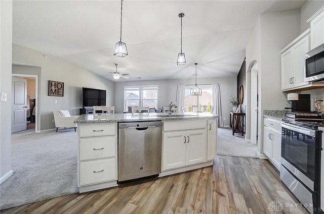 kitchen featuring appliances with stainless steel finishes, open floor plan, vaulted ceiling, white cabinetry, and a sink