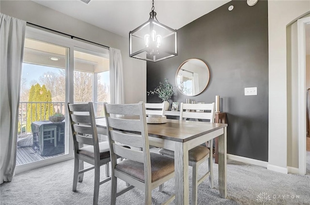 carpeted dining area with a chandelier and baseboards