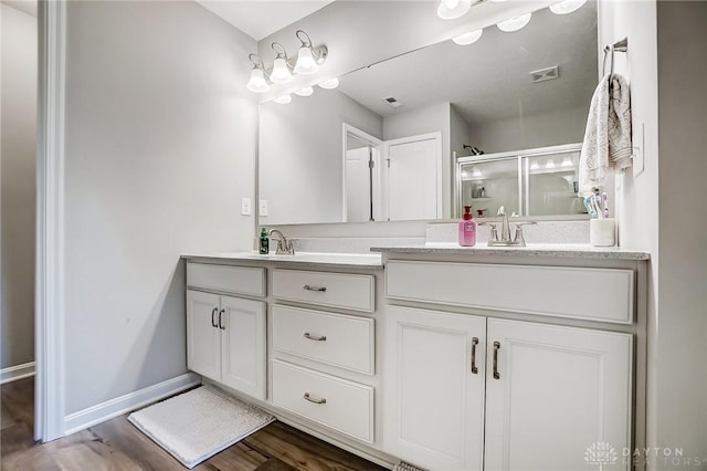 bathroom featuring double vanity, wood finished floors, a sink, and a shower stall