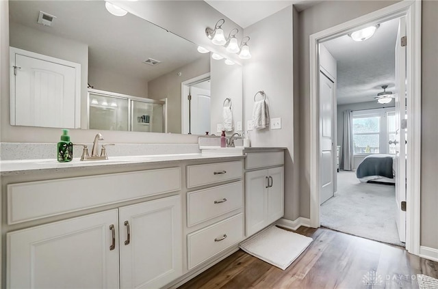 ensuite bathroom featuring double vanity, a stall shower, a sink, and wood finished floors