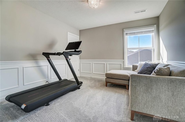 workout area featuring a wainscoted wall, a textured ceiling, visible vents, and carpet flooring