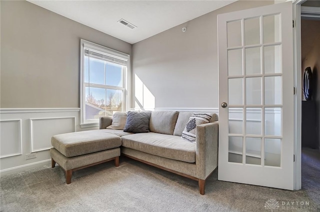 sitting room with carpet, a wainscoted wall, lofted ceiling, visible vents, and a decorative wall