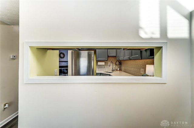 kitchen with tasteful backsplash, light countertops, gray cabinetry, freestanding refrigerator, and a sink