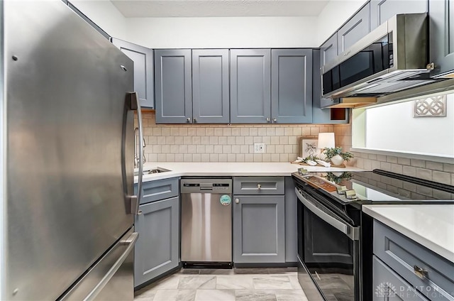 kitchen with tasteful backsplash, stainless steel appliances, light countertops, and gray cabinetry