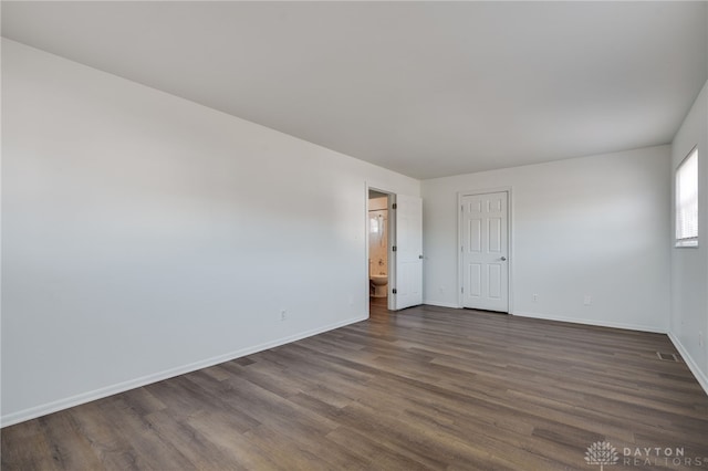 spare room featuring dark wood-type flooring, visible vents, and baseboards