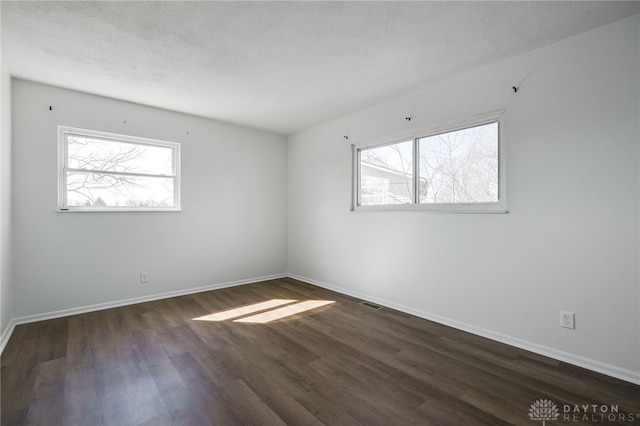 empty room with a healthy amount of sunlight, a textured ceiling, baseboards, and dark wood-type flooring