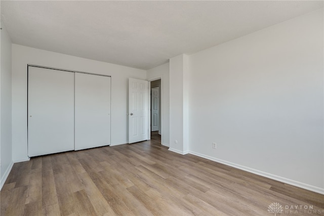 unfurnished bedroom with baseboards, a closet, and light wood-style floors