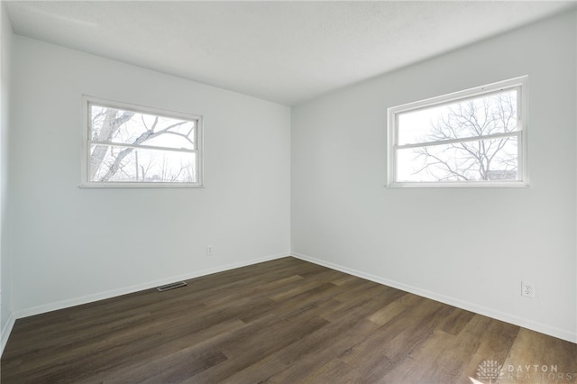 spare room with dark wood-style floors, baseboards, and visible vents