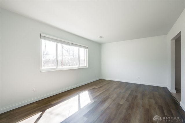 empty room with dark wood-type flooring, visible vents, and baseboards