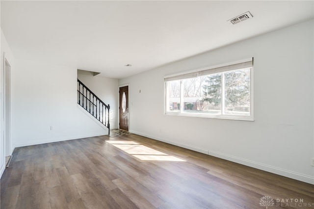 unfurnished living room featuring baseboards, stairs, visible vents, and wood finished floors