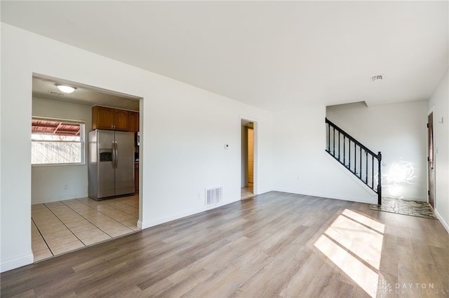 unfurnished living room with stairs, baseboards, visible vents, and light wood-style floors