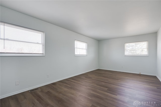 empty room featuring visible vents, dark wood finished floors, and baseboards