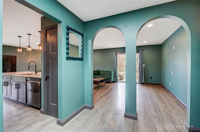 corridor with light wood-style flooring, baseboards, arched walkways, and a sink