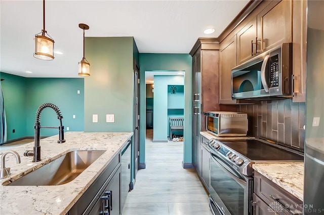 kitchen featuring stainless steel appliances, hanging light fixtures, decorative backsplash, a sink, and light stone countertops