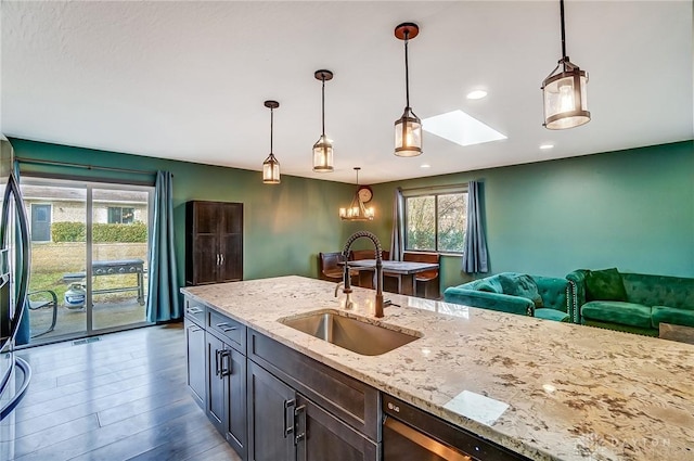 kitchen featuring light stone counters, dark wood-type flooring, a skylight, a sink, and decorative light fixtures