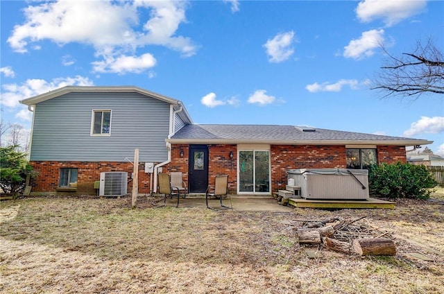 rear view of property with cooling unit, brick siding, a patio, and a hot tub