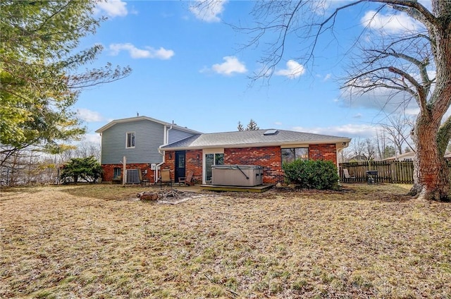 back of property featuring a yard, brick siding, fence, and a hot tub