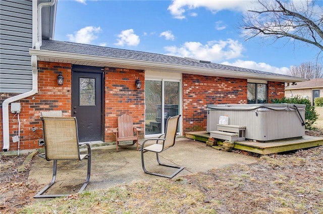 rear view of house featuring a patio, brick siding, a shingled roof, and a hot tub