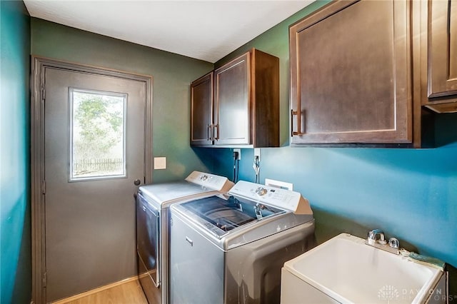 laundry area featuring washing machine and dryer, a sink, cabinet space, and light wood-style floors