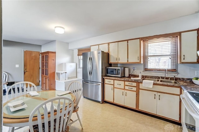 kitchen featuring a sink, appliances with stainless steel finishes, cream cabinetry, light floors, and dark countertops