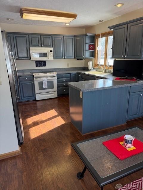 kitchen with a peninsula, white appliances, a sink, and dark wood-type flooring