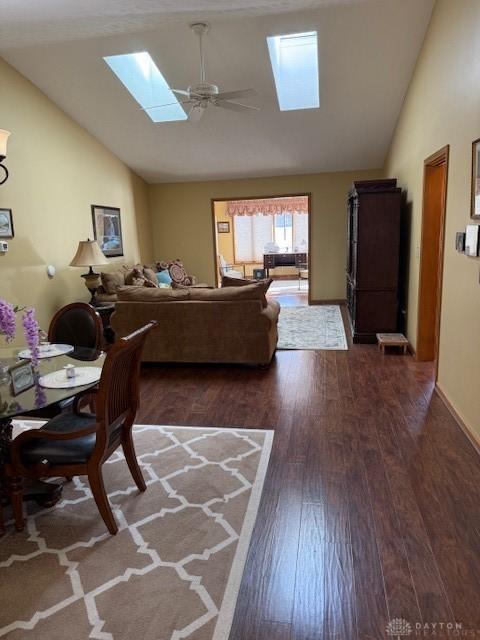 living area with vaulted ceiling with skylight, baseboards, dark wood finished floors, and a ceiling fan