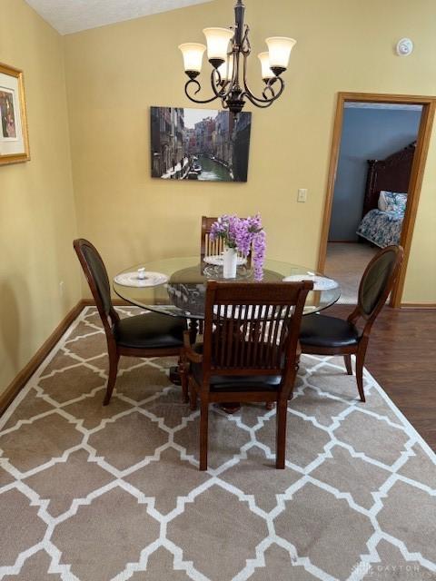 dining room with lofted ceiling, baseboards, a notable chandelier, and wood finished floors