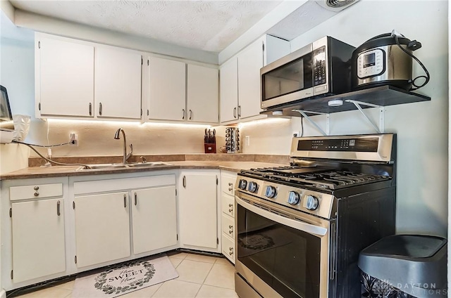 kitchen with appliances with stainless steel finishes, a textured ceiling, white cabinetry, a sink, and light tile patterned flooring