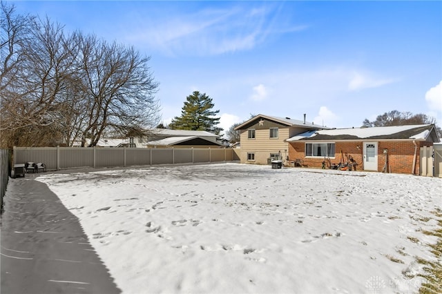 snow covered rear of property with fence and brick siding