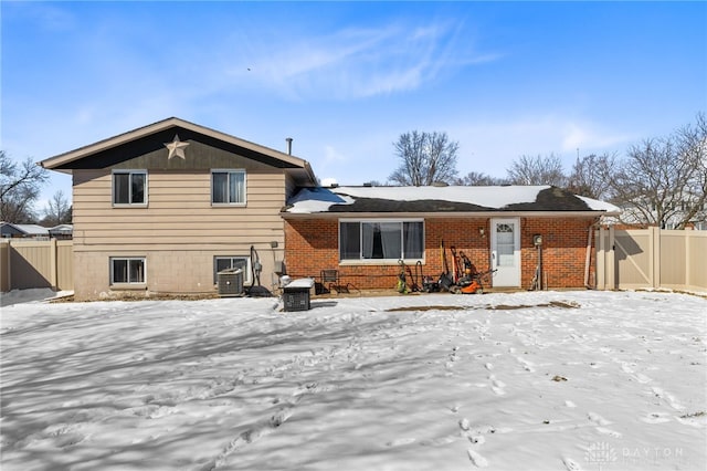 snow covered house with fence, cooling unit, and brick siding