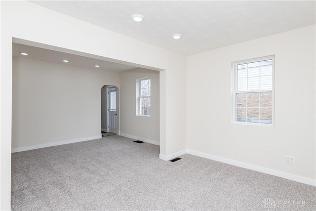 empty room featuring light carpet, plenty of natural light, visible vents, and baseboards