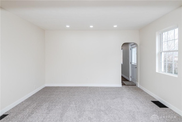 carpeted empty room featuring arched walkways, visible vents, baseboards, and recessed lighting