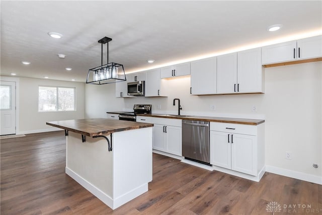 kitchen featuring stainless steel appliances, hanging light fixtures, white cabinets, a sink, and butcher block countertops