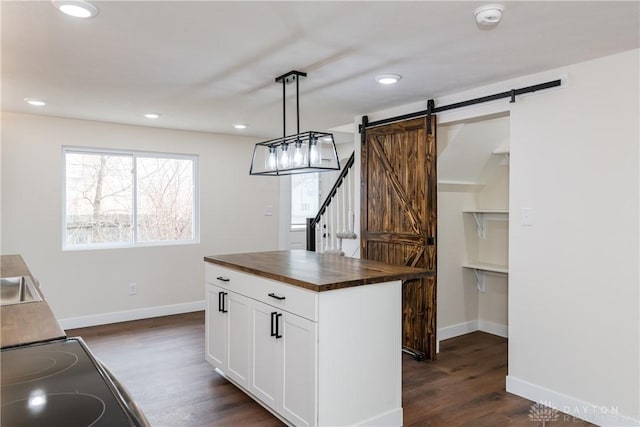 kitchen with a barn door, wood counters, white cabinets, hanging light fixtures, and a center island