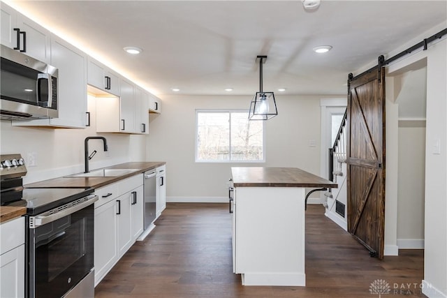 kitchen featuring hanging light fixtures, a barn door, appliances with stainless steel finishes, white cabinetry, and butcher block countertops