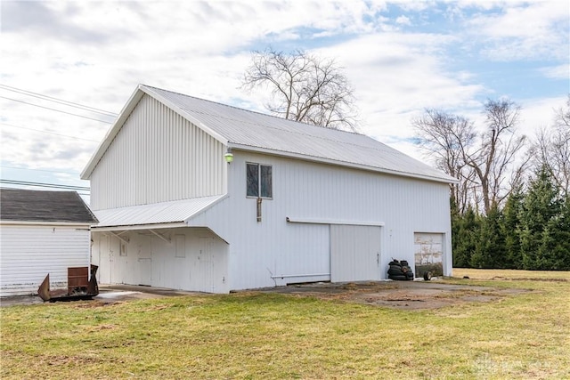 rear view of property with a detached garage, metal roof, a lawn, and an outdoor structure