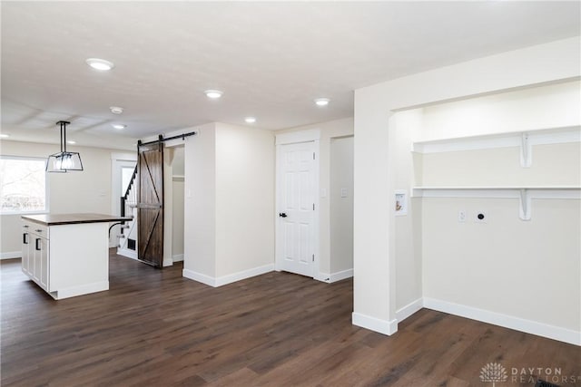 interior space featuring a barn door, baseboards, dark wood finished floors, decorative light fixtures, and white cabinetry