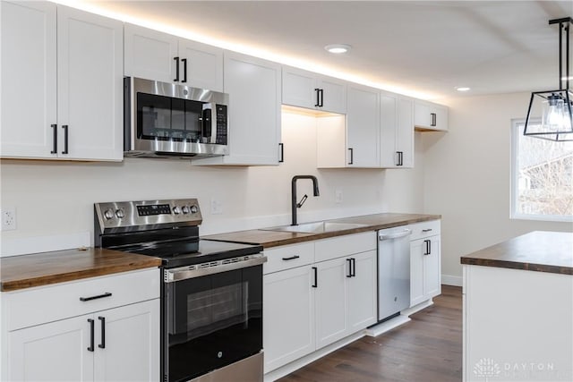 kitchen with hanging light fixtures, butcher block countertops, a sink, and appliances with stainless steel finishes