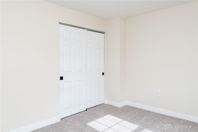 unfurnished bedroom with light carpet, a closet, and baseboards