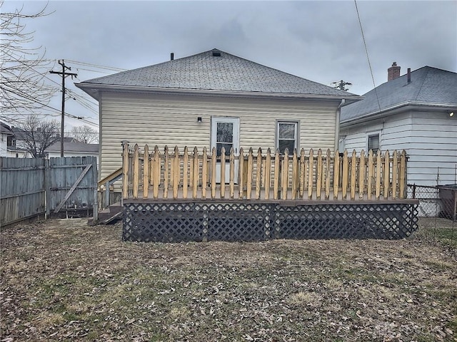 rear view of property with roof with shingles, fence, and a wooden deck