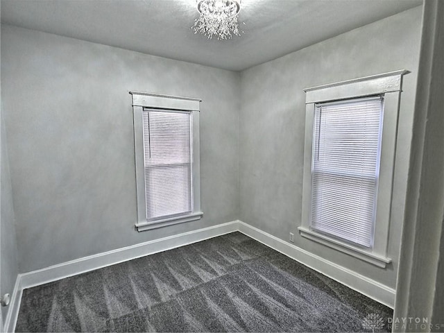 empty room featuring dark carpet, an inviting chandelier, and baseboards