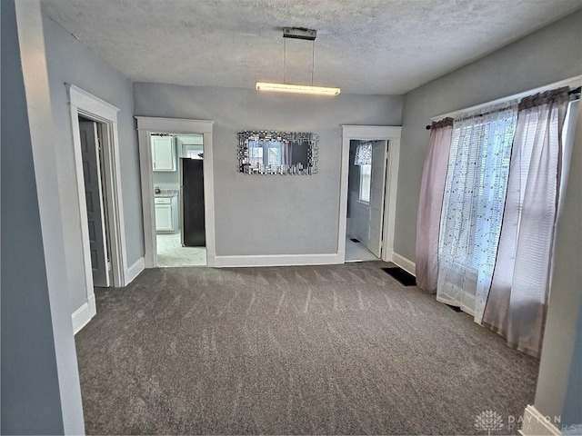 unfurnished room with a textured ceiling, carpet floors, and baseboards